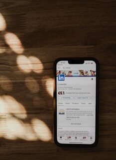 Smartphone on a wooden table showing LinkedIn app in natural light.